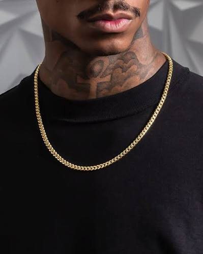 Man wearing a gold Cuban link chain over a black shirt, showing the flat interlocked links